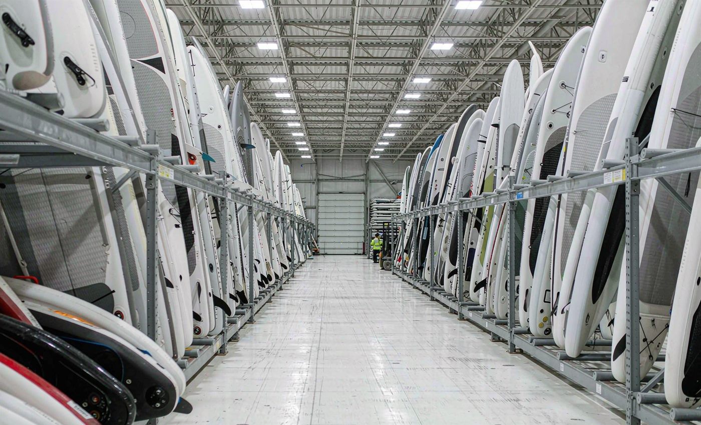 Finished paddleboards and kayak hulls standing in a warehouse aisle